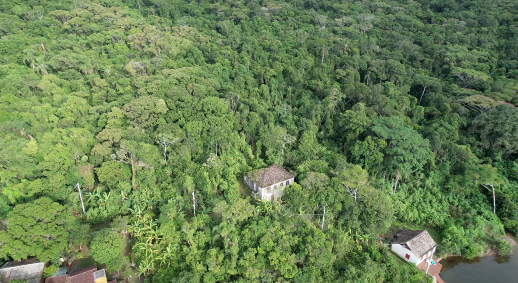 imagem do Casarão rodeado de floresta. está localizado a poucos metros da Lagoa da Conceição, onde na beira se encontra um engenho de farinha desativado.